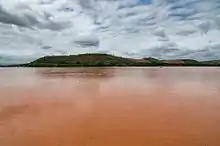 Muddy floodwaters in an open area with a tree-covered hill in the background