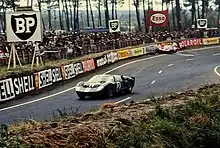 The #2 GT40 of McLaren/Amon passes the wrecked #14 GT40 of Spoerry/Sutcliffe at the Esses.