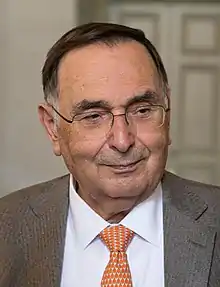 Giampaolo Dallara wearing a Tan blazer, white buttoned-up shirt and a orange tie
