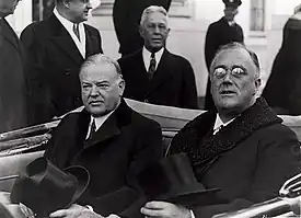 Hoover and Roosevelt sit in the back seat of an open top car with their hats on their laps.
