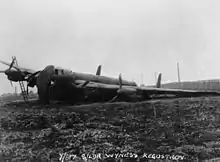 A black and white photo of a large monoplane aircraft with four propeller engines on muddy ground. The aircraft's port-side landing gear is not working, and it is lying at a steep angle with a tarpaulin over its nose.