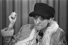 Young seated woman in a black cap, holding a cigarette