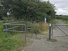 A metal barrier crosses the path, with a chicane and bar at ankle height.