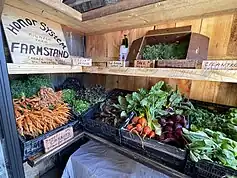 All wooden boxes stand with two-levels. They have wooden signs in cursive letters with details of what is being on display, with prices. The vegetables are a mixture of carrots, beets, cilantro, lettuce, and dill.