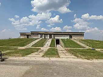 The front façade of a two-0story stucco building. The ground floor is covered by an earthen berm.