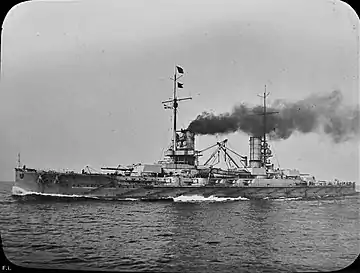 A World War I-era battleship at sea; her two funnels are emitting a large amount of smoke