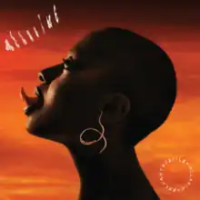 A profile shot of Salvant with her tongue sticking out in front of a brown and orange backdrop