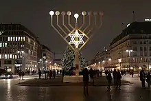 A large Hanukkah menorah with a Christmas tree visible in the background