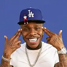 Cover art depicting DaBaby smiling and pointing finger guns at his head. He wears a baseball hat and a smaller version of himself is sitting on the brim.