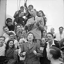 Photograph of Ingham with Formby entertaining the crew of HMS Ambitious, off the Normandy coast in 1944