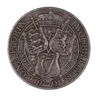 The reverse of a 1901 British Florin, featuring the heraldic shields of England, Scotland, and Ireland arranged in a triangular formation around a thistle, shamrock, and rose. A royal crown is placed above, bordered by two scepters crossed at the center of the shields and coin.  The date at bottom, 1901, is interrupted by the bottom of the Irish shield. Arcing around the coin at left is ONE FLORIN, while at right is TWO SHILLINGS.