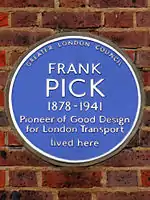 A circular blue ceramic plaque with white raise lettering fixed to a brick wall bears the text "FRANK PICK, 1878–1941 Pioneer of Good Design for London Transport lived here"