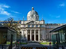 Building with central cupola and Ionic columns, with modern gatehouses in foreground