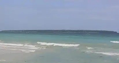 Long low green island, about 3.9&nbsp;km (2&nbsp;mi) distant.  Two beaches can be made out.