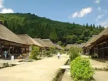 Street lined by similar wooden houses with white walls and thatched roofs.