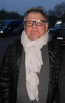 Photo of Janusz Kamiński wearing a white scarf and a black bubble vest in 2014.