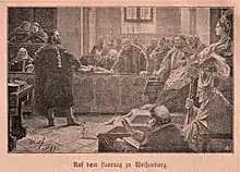 In a room filled with people, a bearded man is standing before a crowned woman who sits on a throne and is surrounded by Catholic priests