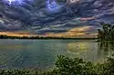 Gray storm clouds roll over green trees and plants that rim a choppy gray lake