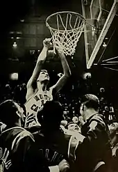 A basketball player cutting a net away from the rim.