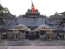A cemetery with densely packed headstones made of cement. Almost no grass or flora can be seen. Many of the headstones are elaborate with a yellow or orange-tiled roof in the manner of an East Asian temple