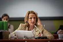 A blonde woman speaking at a meeting