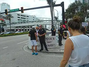 Counter-protester with "Gays for Trump" and "Impeach Nazi Democrats" signs confronted by a protester in Hollywood, Florida