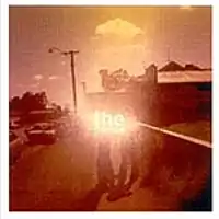 A sepia-toned shot of a street scene. Two people standing in the middle on a footpath are partly obscured by the brightened image of the group's name. To the right is the side of a shop or a house with an advert on the brickwork. To the left is a roadway with cars parked, one of which has the driver's door open.