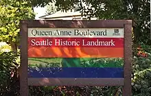 photograph of a sign created by the Parks and Recreation department for Queen Anne Boulevard. It has horizontal stripes in cream, red, orange, green, and blue (from top to bottom)