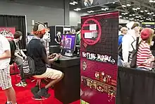 A man playing a demo version of Hotline Miami 2: Wrong Number at a RTX 2014 booth.