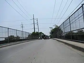 Steel pole 234 (of anchor or flag design) near Tulaoc Overpass in San Simon, Pampanga. Note that it uses NAPOCOR-era steel pole 228. The line also zig-zags which passes through residential areas on this portion instead of directly along NLEX due to the Tulaoc Overpass and  to bypass the TransCo right-of-way and lands or locations for poles 233 and 234 (233 and 234 under TransCo plan of the relocation project located between NGCP-acquired and designated poles 233 and 234, and 234 and 235, respectively) as the ROWs or portions of relocated San Simon–Pulilan segment of the line that use steel poles and lands where they are located (228–254, 257–265, 268–289) were designated and acquired by NGCP thus they are owned, operated, and maintained by it.