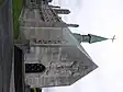 A grey-white stone chapel seen from the northwest, with a central spirelet with a cross. There is an elaborate carving of the Crucifixion over the west door, a tall pinnacle at the corner, and elaborate stone tracery in the windows along the side